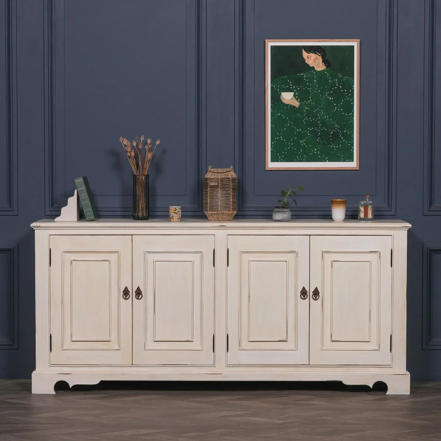 Cream sideboard cabinet with paneled doors against navy wall, decorated with books and vases