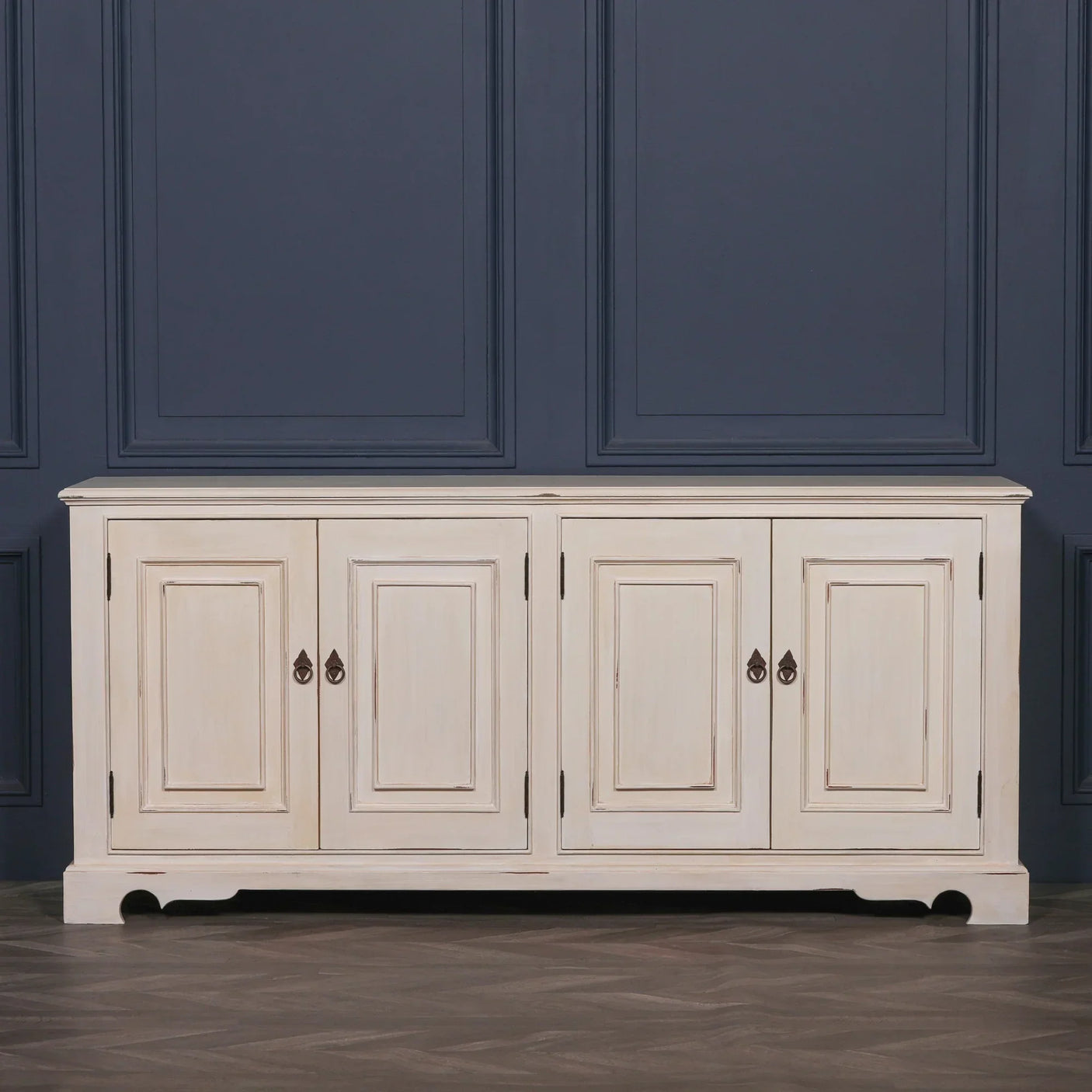Distressed cream wood sideboard with four paneled doors and metal handles against navy wall