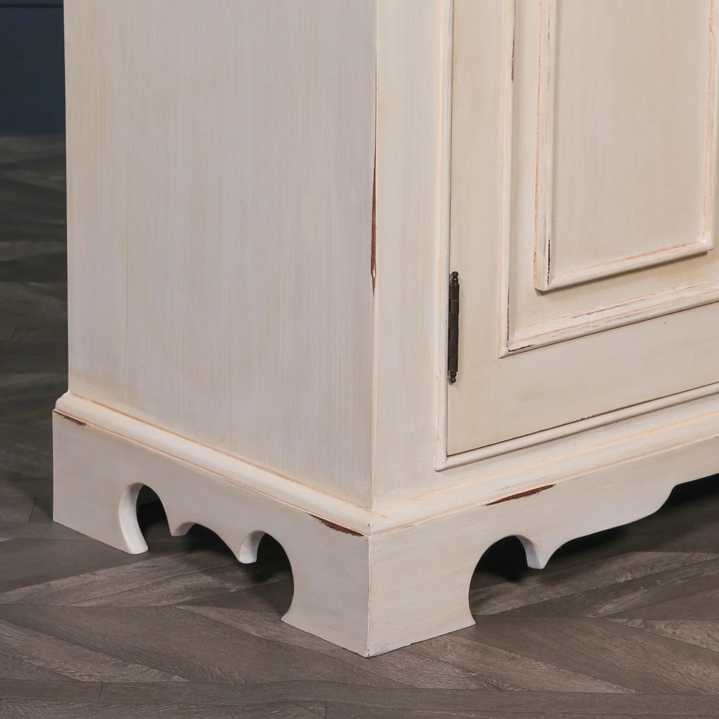Distressed cream wood cabinet base with scalloped detail and paneled door corner view