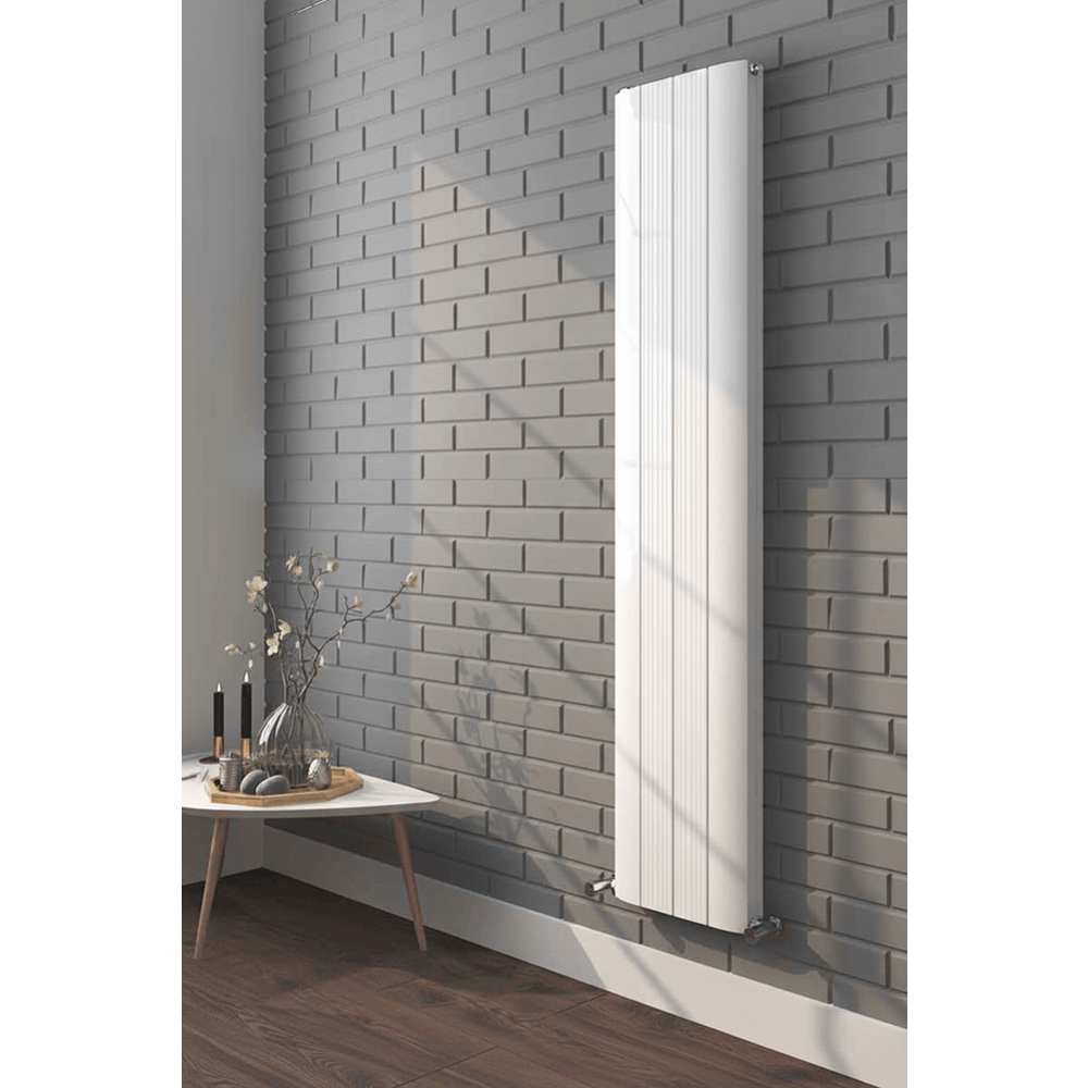 White vertical radiator on a gray brick wall with a small table and decorative items below.