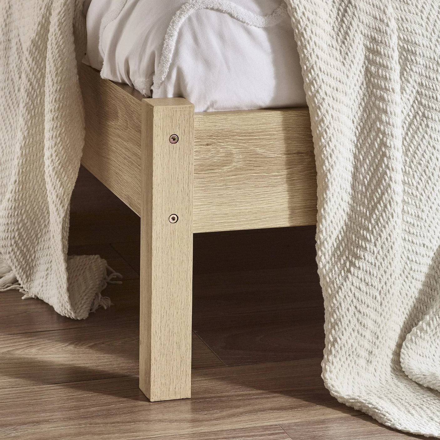 Oak rattan double bed frame corner detail on wooden floor with cream blanket and bedding