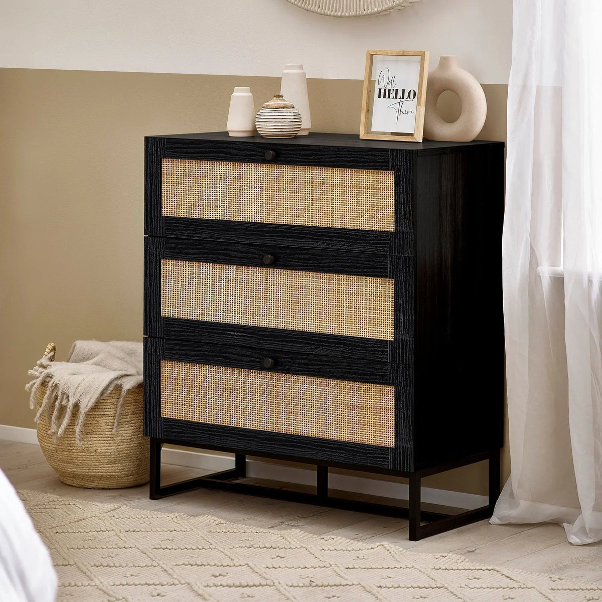 Black wooden 3 drawer chest with rattan fronts in modern bedroom setting