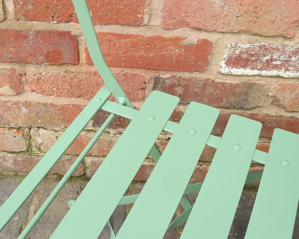 Olive green metal garden chair slats with brick wall background, showing close-up detail