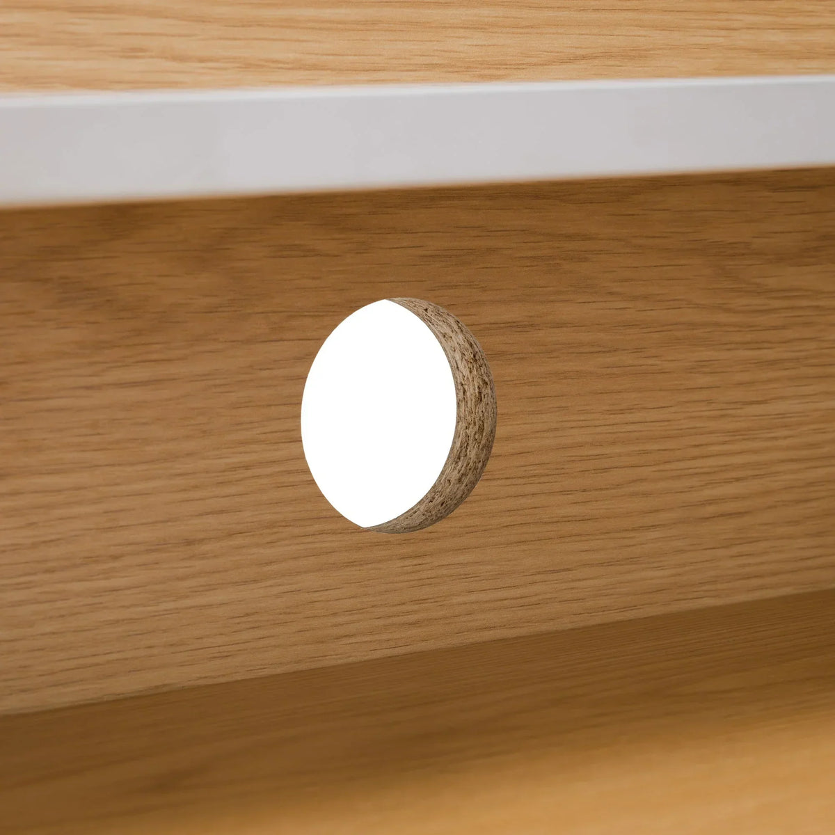 Oak desk cable management hole with white trim detail on wooden panel