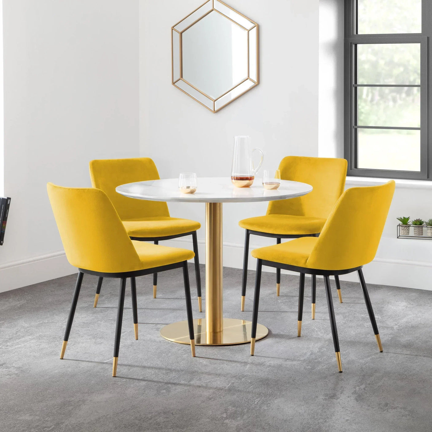 Round marble dining table with gold base and four yellow velvet chairs in modern room