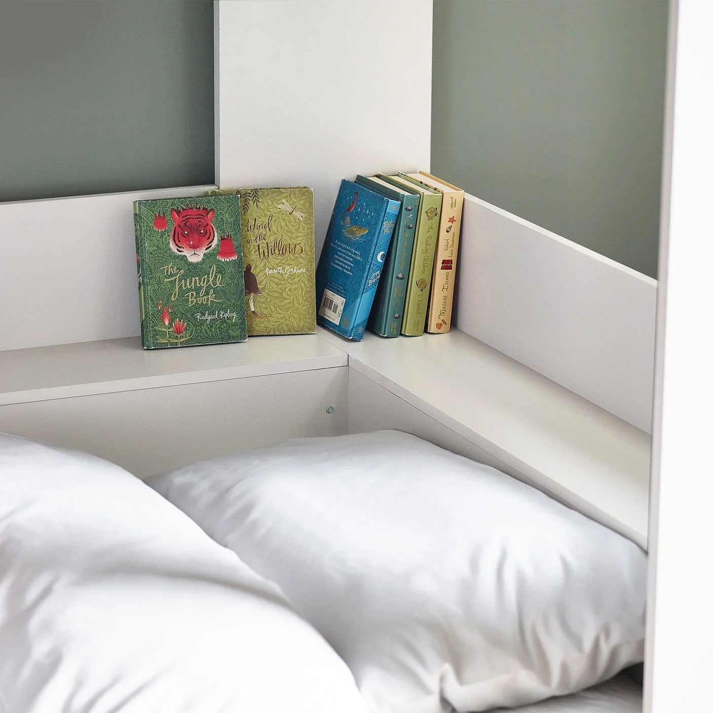 White bunk bed with built-in shelf holding books and white pillows in closeup view