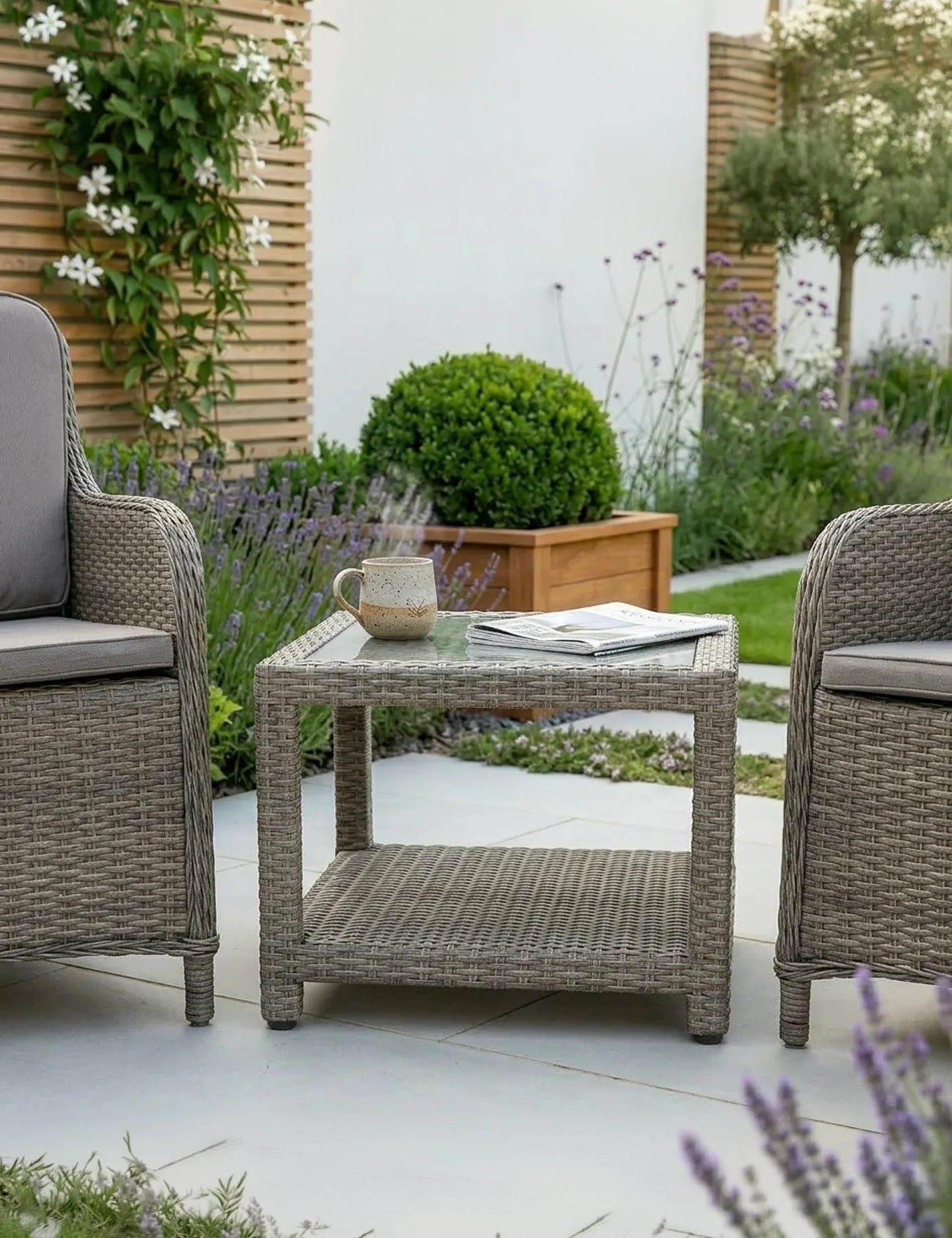 Rattan garden coffee table with glass top arranged on patio between two chairs