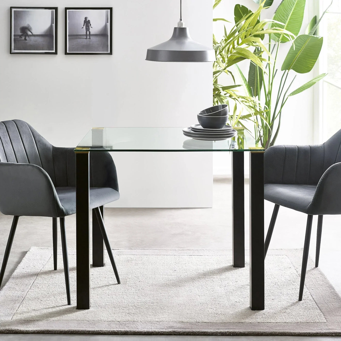 Glass square dining table with black legs and grey chairs in modern room setting