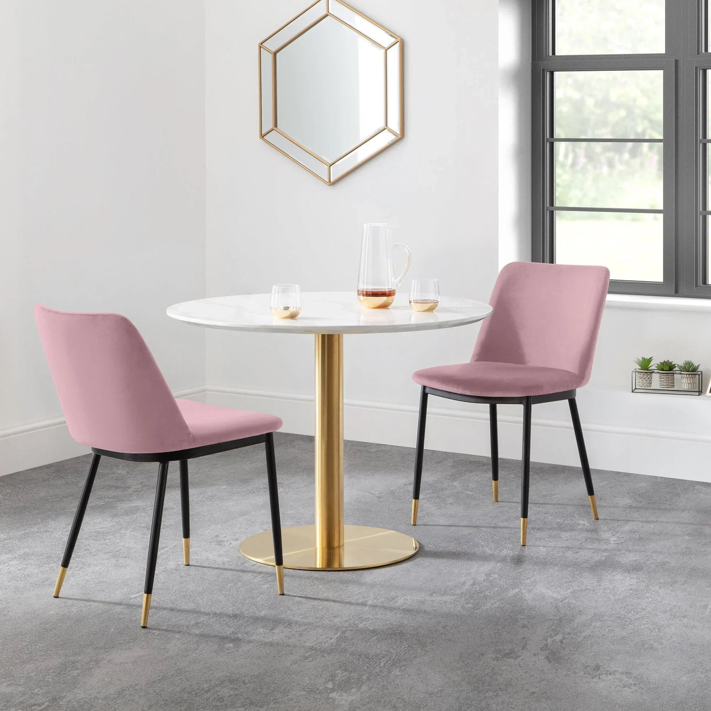 Round marble dining table with gold base and two pink chairs in modern bright dining room