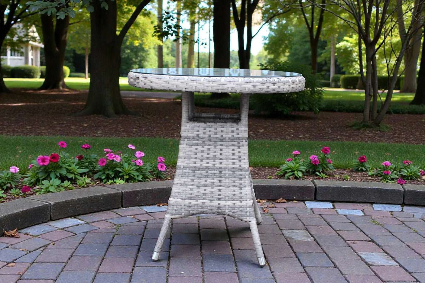 Round rattan garden bistro table with glass top on patio surrounded by flowers