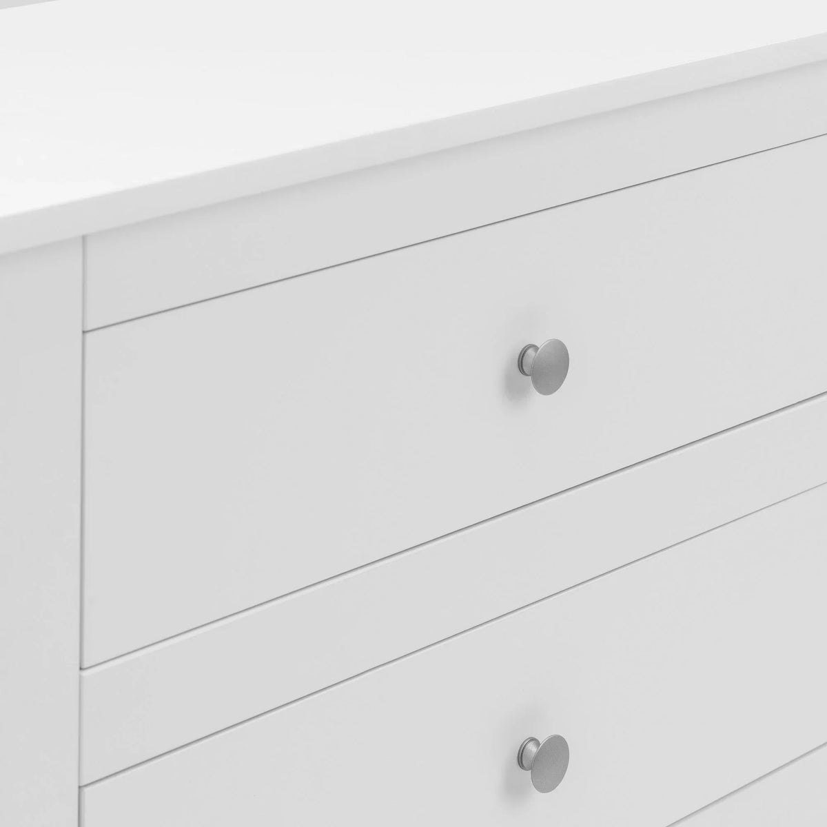 White chest of drawers with silver handles, closeup on drawer fronts and top surface