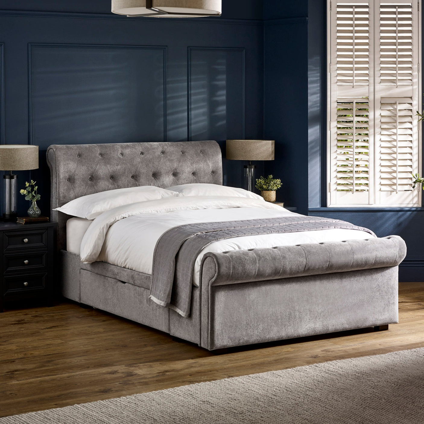 Upholstered grey fabric double bed with tufted headboard and footboard in a dark blue room.