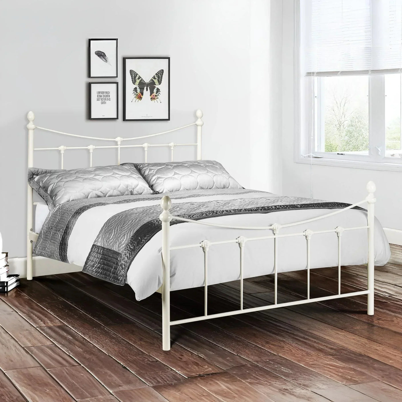 Stone white metal double bed with grey bedding in bright bedroom with wood floor