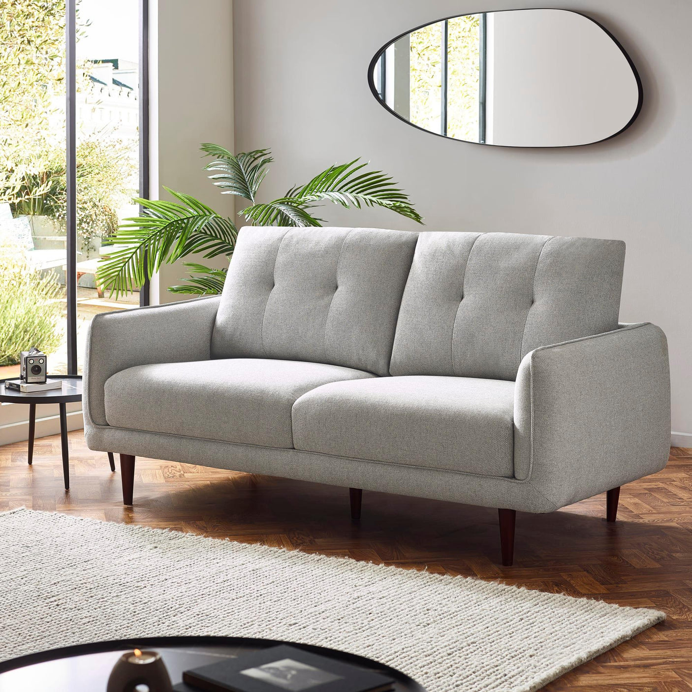 Light grey fabric sofa with tufted cushions in modern living room with wooden flooring