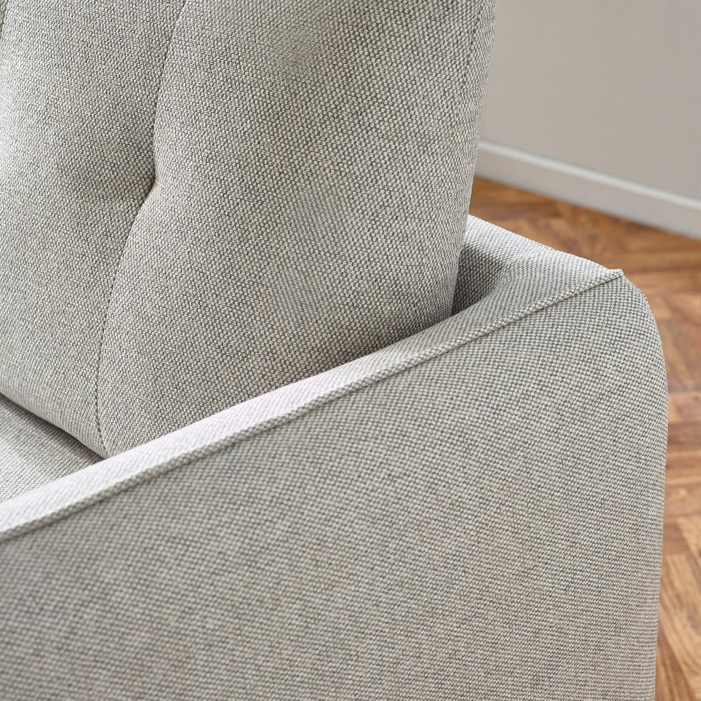 Close-up of grey fabric sofa arm and tufted backrest detailing on wooden floor