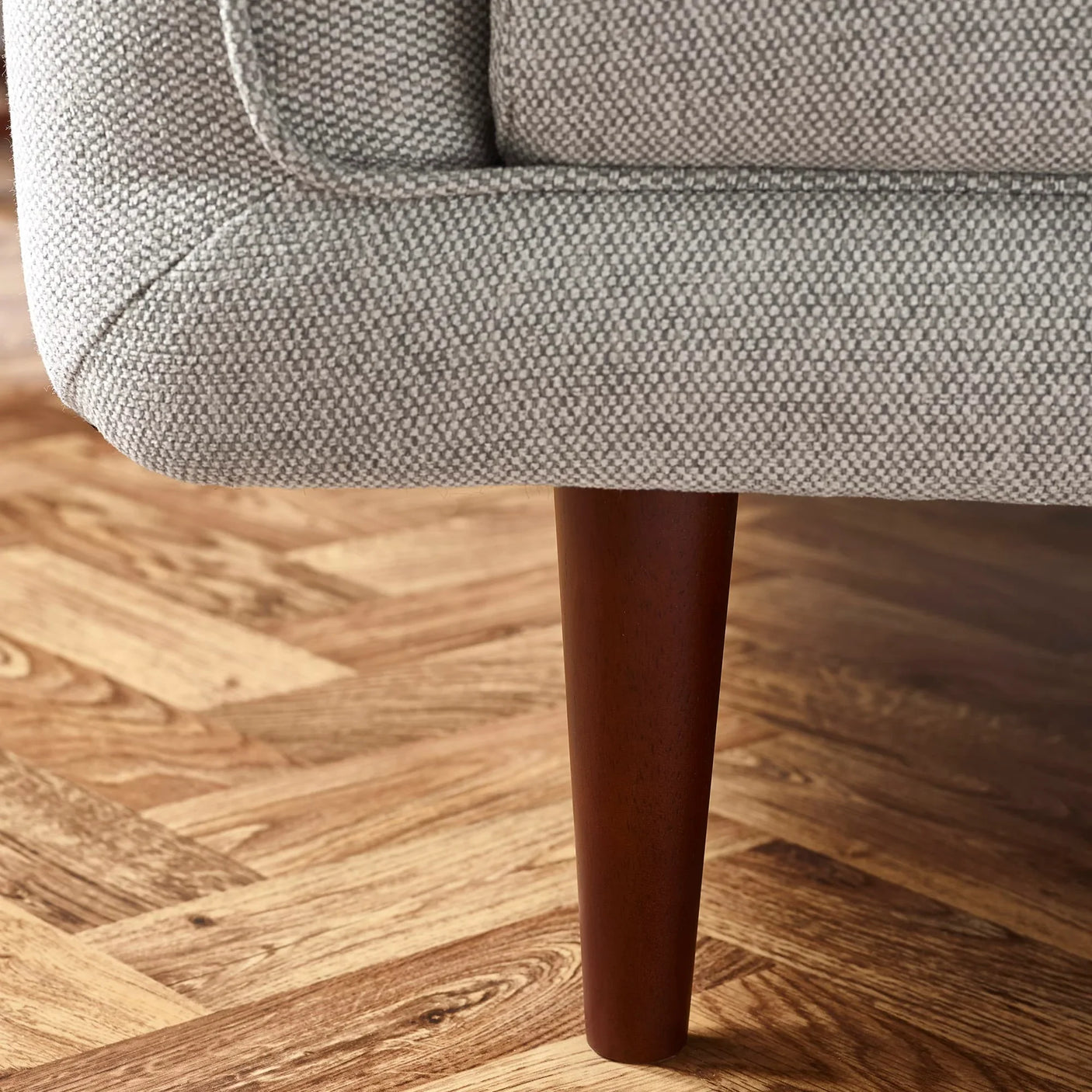 Closeup of grey fabric sofa corner with wooden leg on herringbone floor