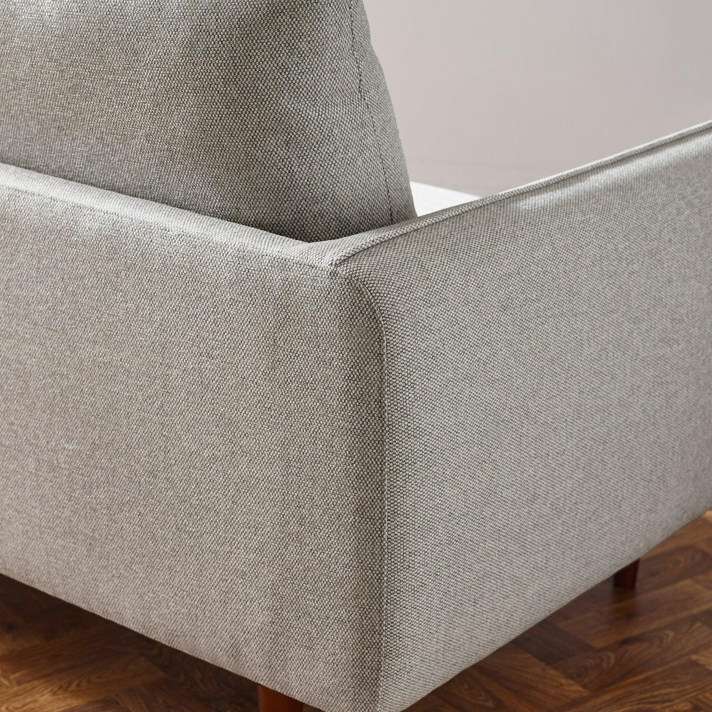 Close-up of grey fabric sofa arm and cushion with wooden floor background