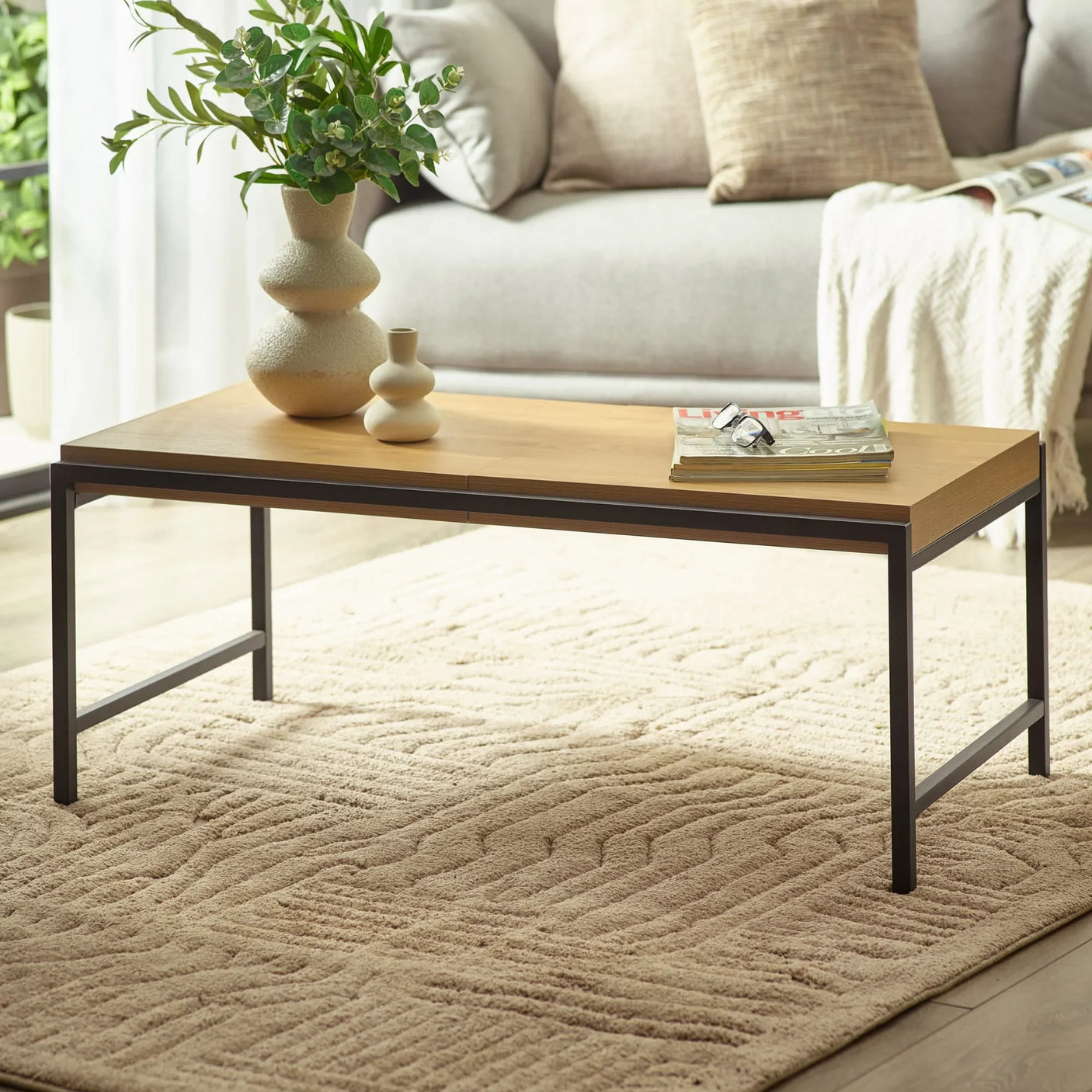 Wooden coffee table with black metal frame, vases, magazines, and plant in modern living room