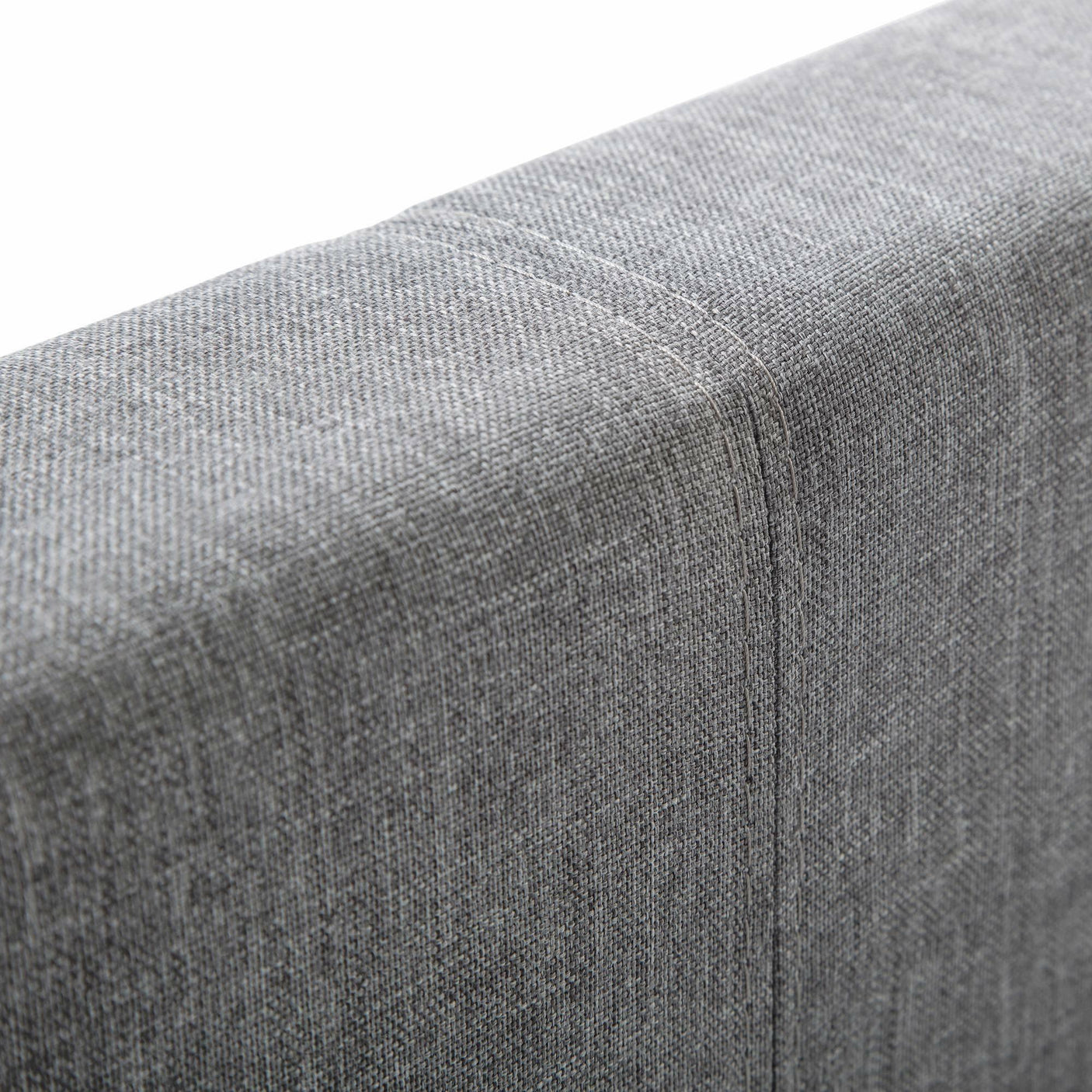 Detail of light grey linen king bed headboard upholstery with visible stitching
