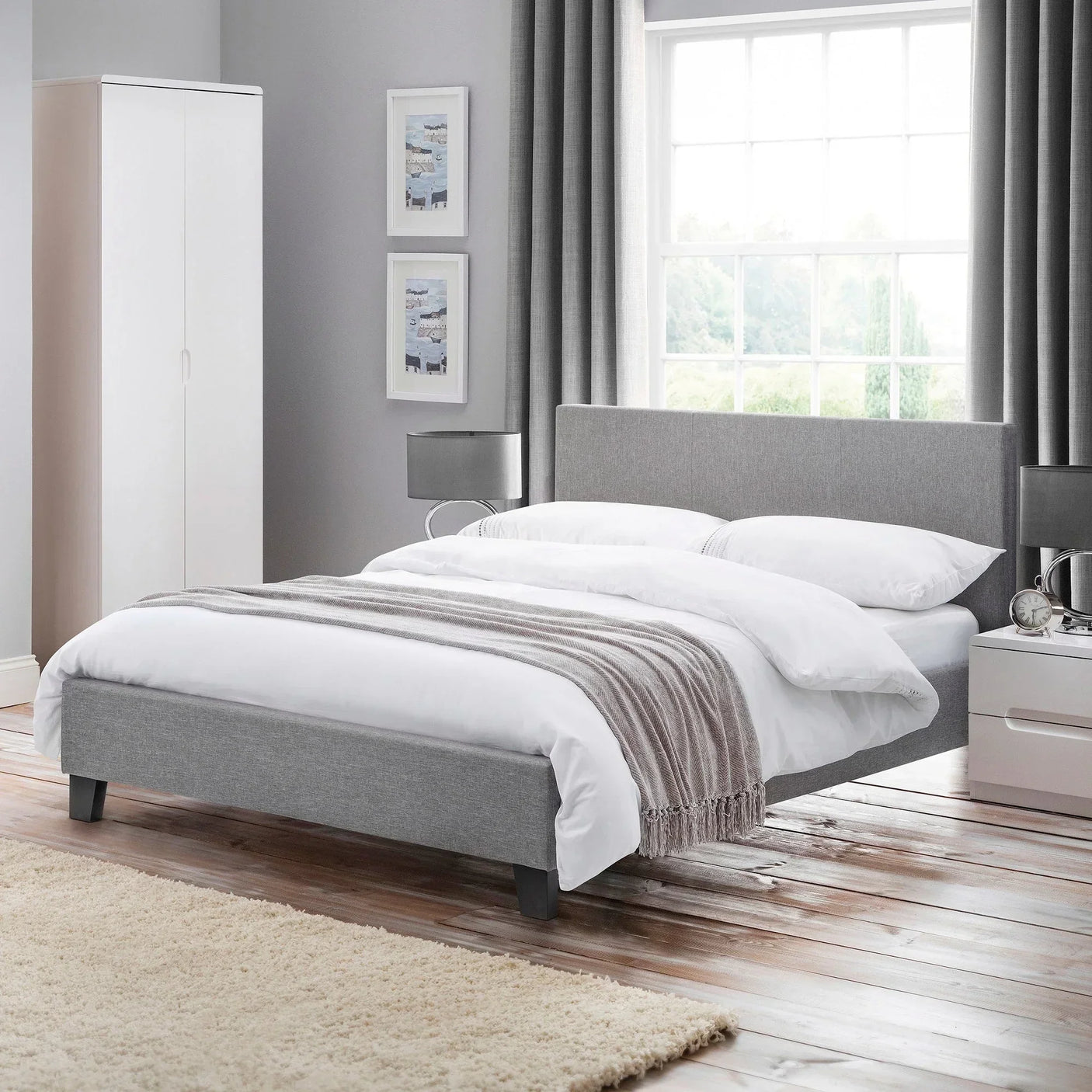 Grey upholstered bed frame with white bedding in modern bedroom with wardrobe and bedside tables