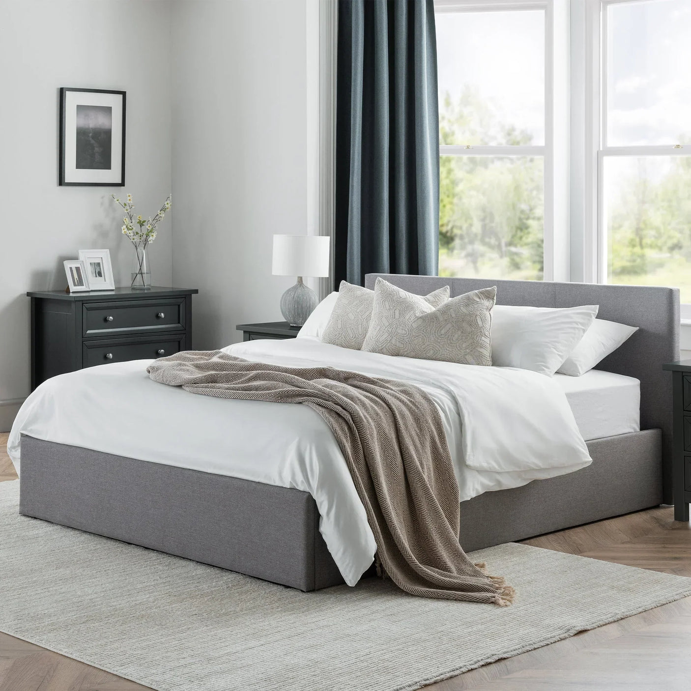 Grey lift-up storage bed with headboard in modern bedroom, white bedding and beige throw blanket