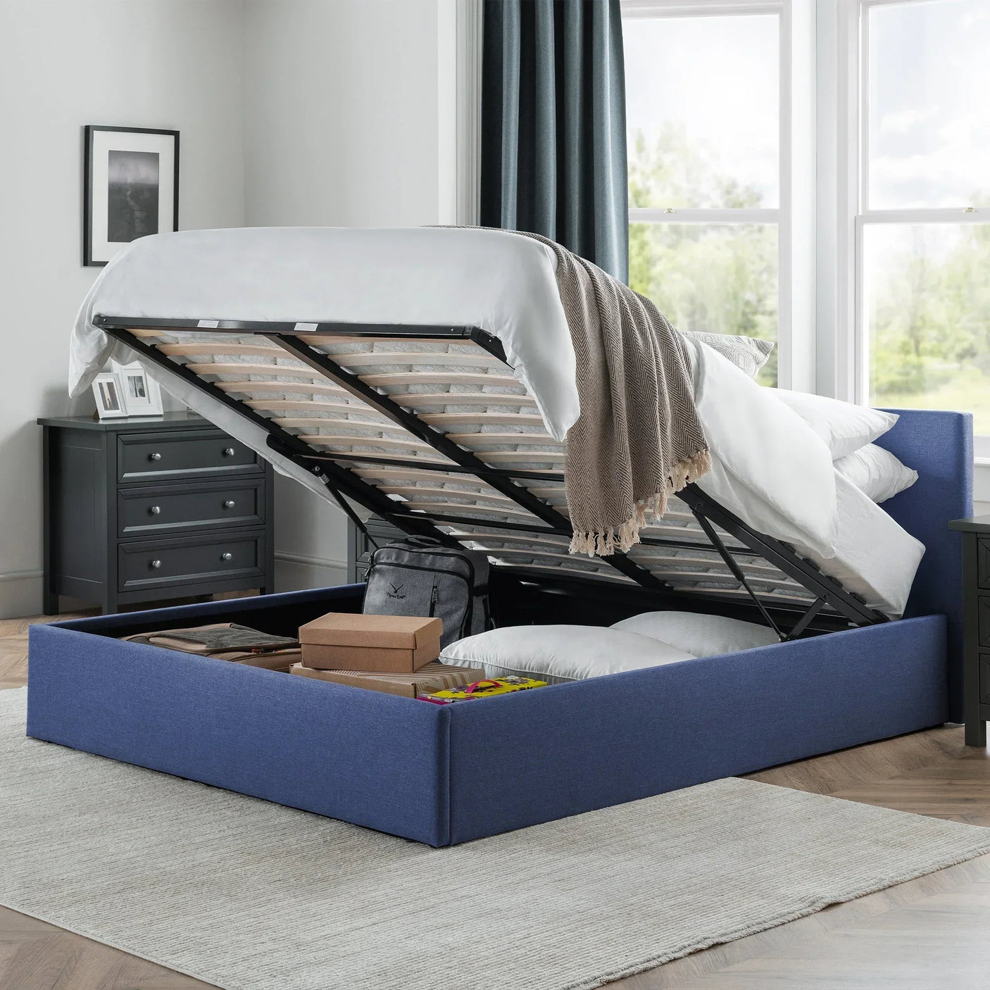 blue lift-up storage bed with open base showing pillows and boxes in modern bedroom
