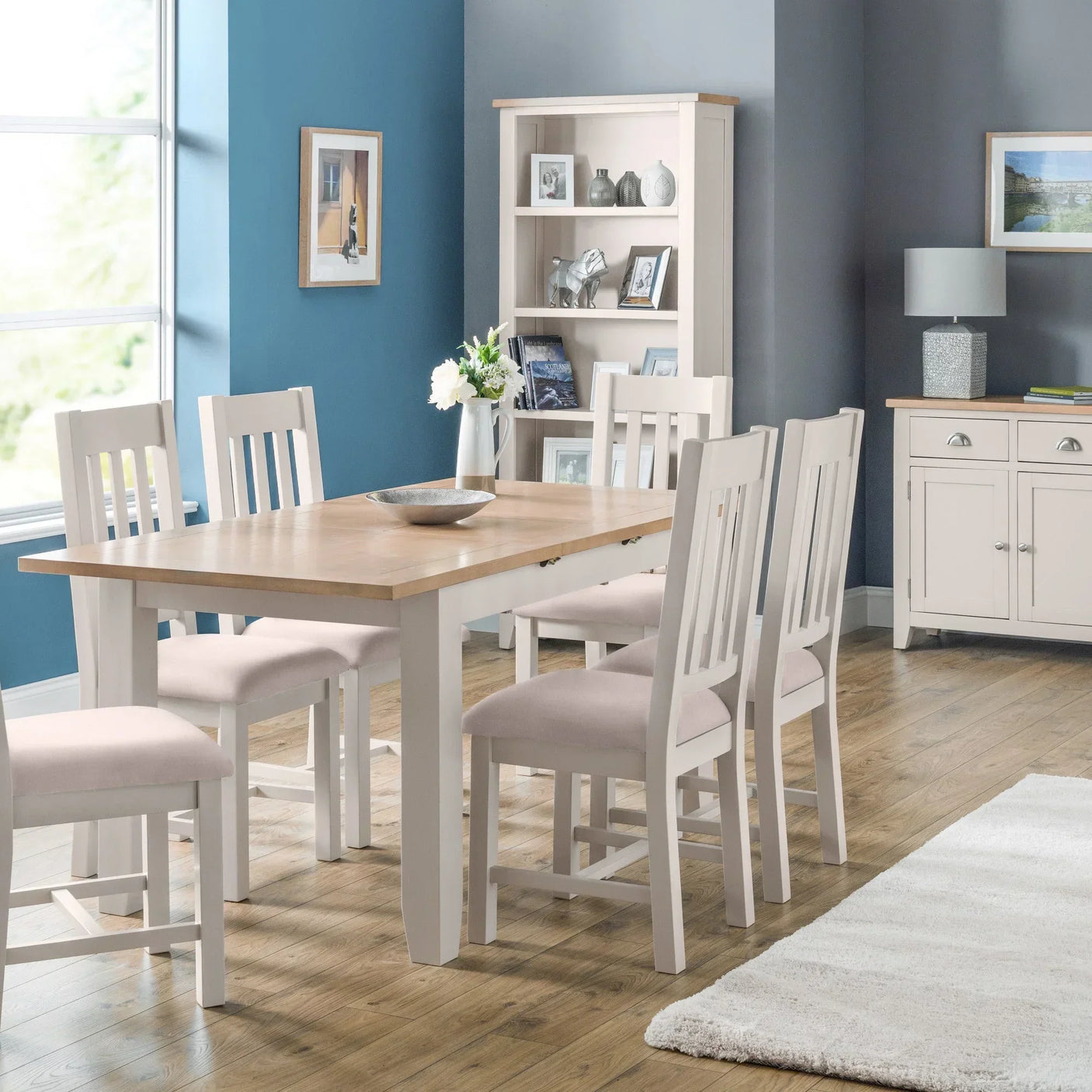 Wood dining table set with six cream chairs in modern dining room with shelving unit