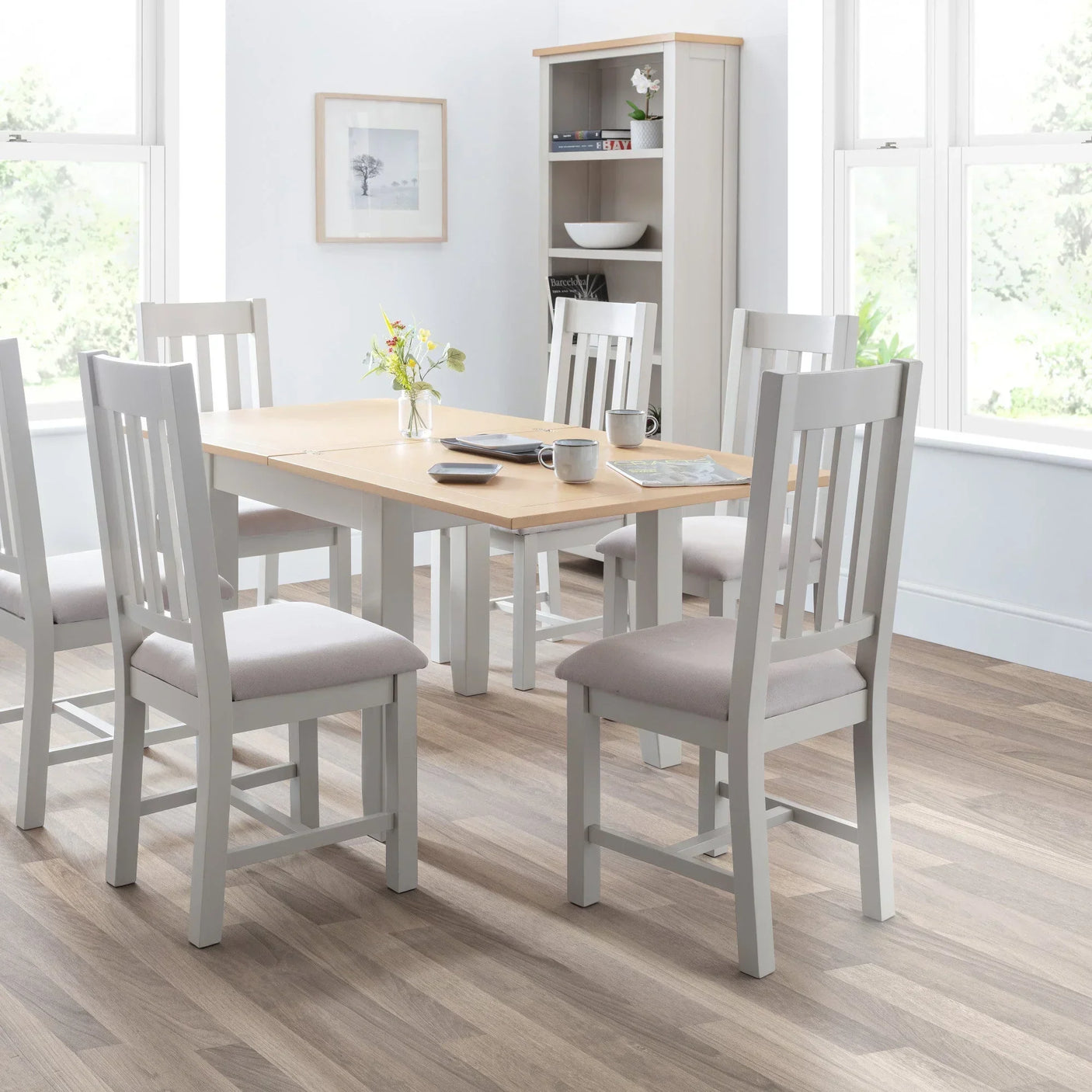 Light wood dining table with six grey chairs in a bright modern dining room setting
