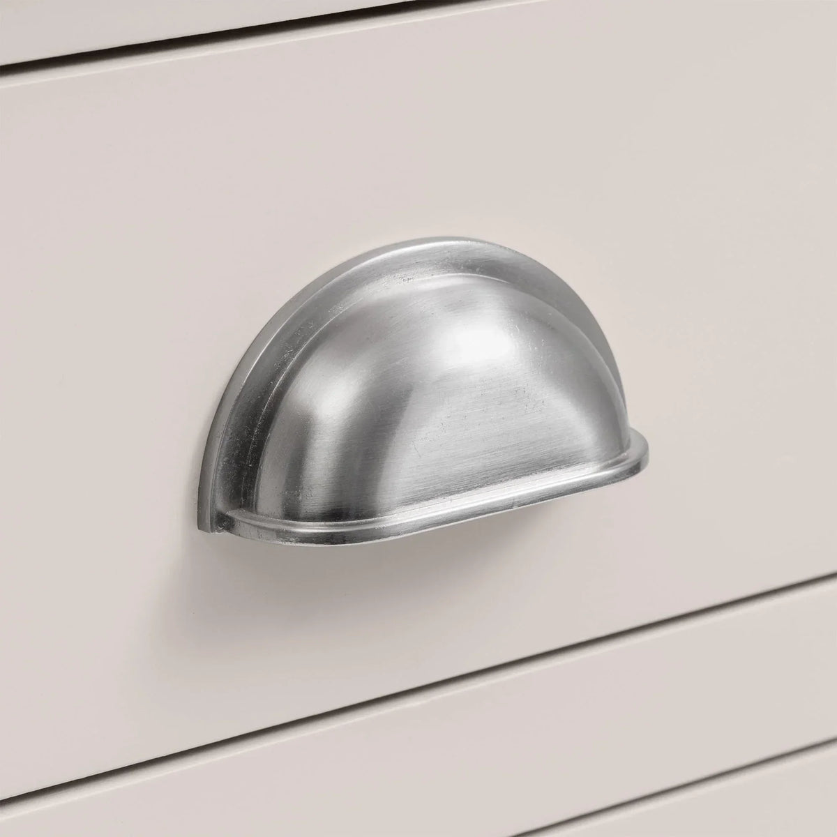 Silver cup handle on white wooden bedside table drawer close-up