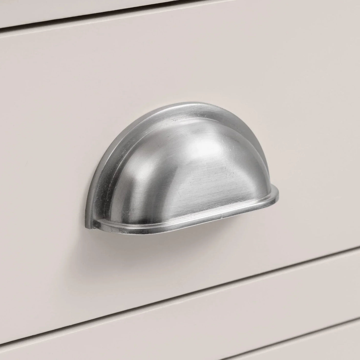 Brushed metal cup handle on cream painted drawer front for furniture cabinet