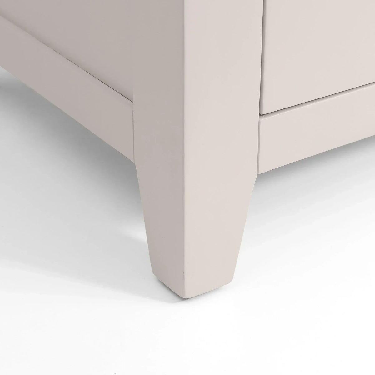 Close view of painted wood chest of drawers leg with smooth light grey finish