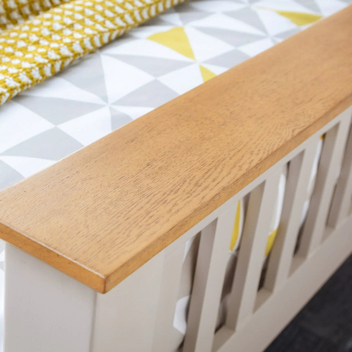 Closeup of wooden bed frame footboard with geometric bedding and yellow throw