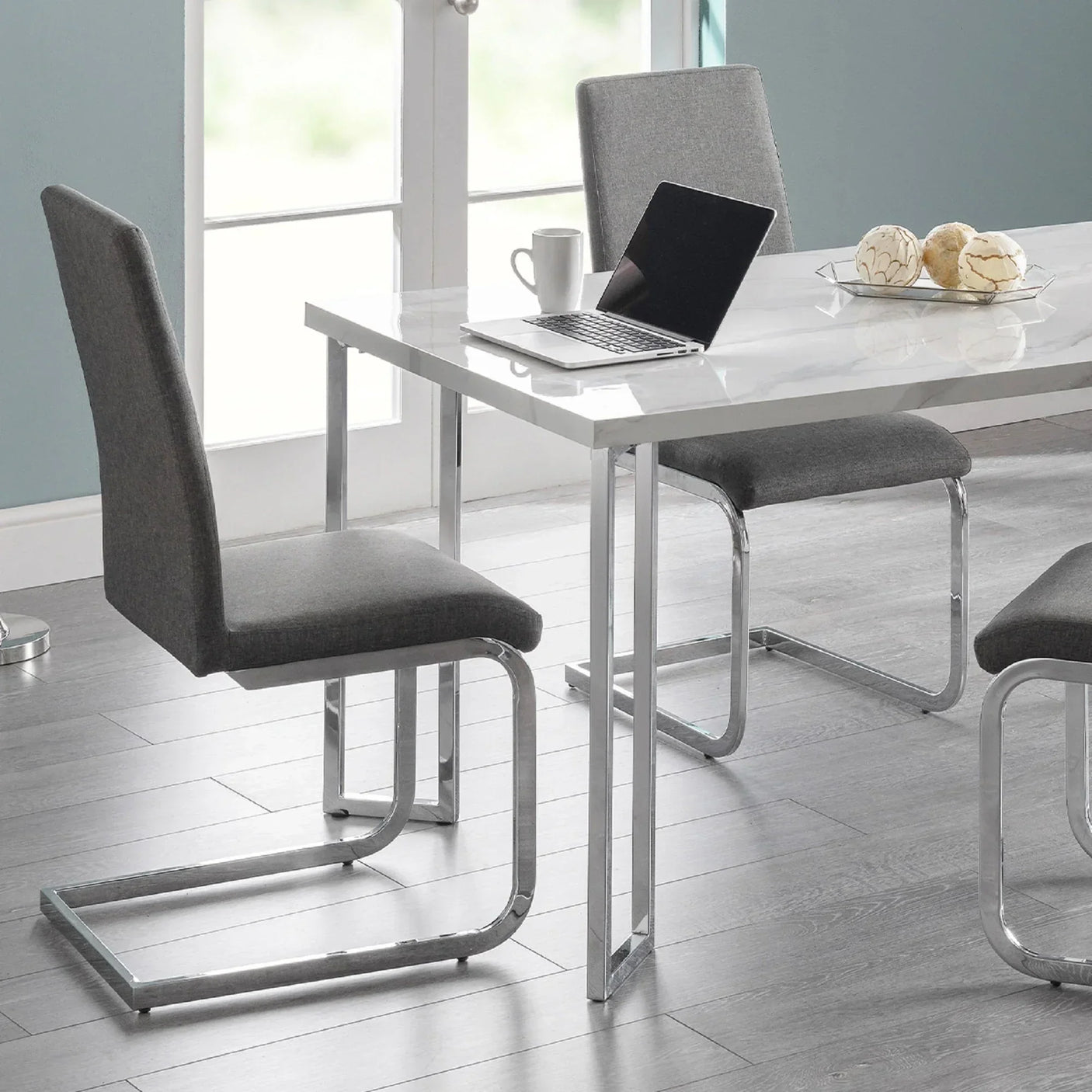 Grey dining chairs with chrome legs around rectangular white dining table on wood floor