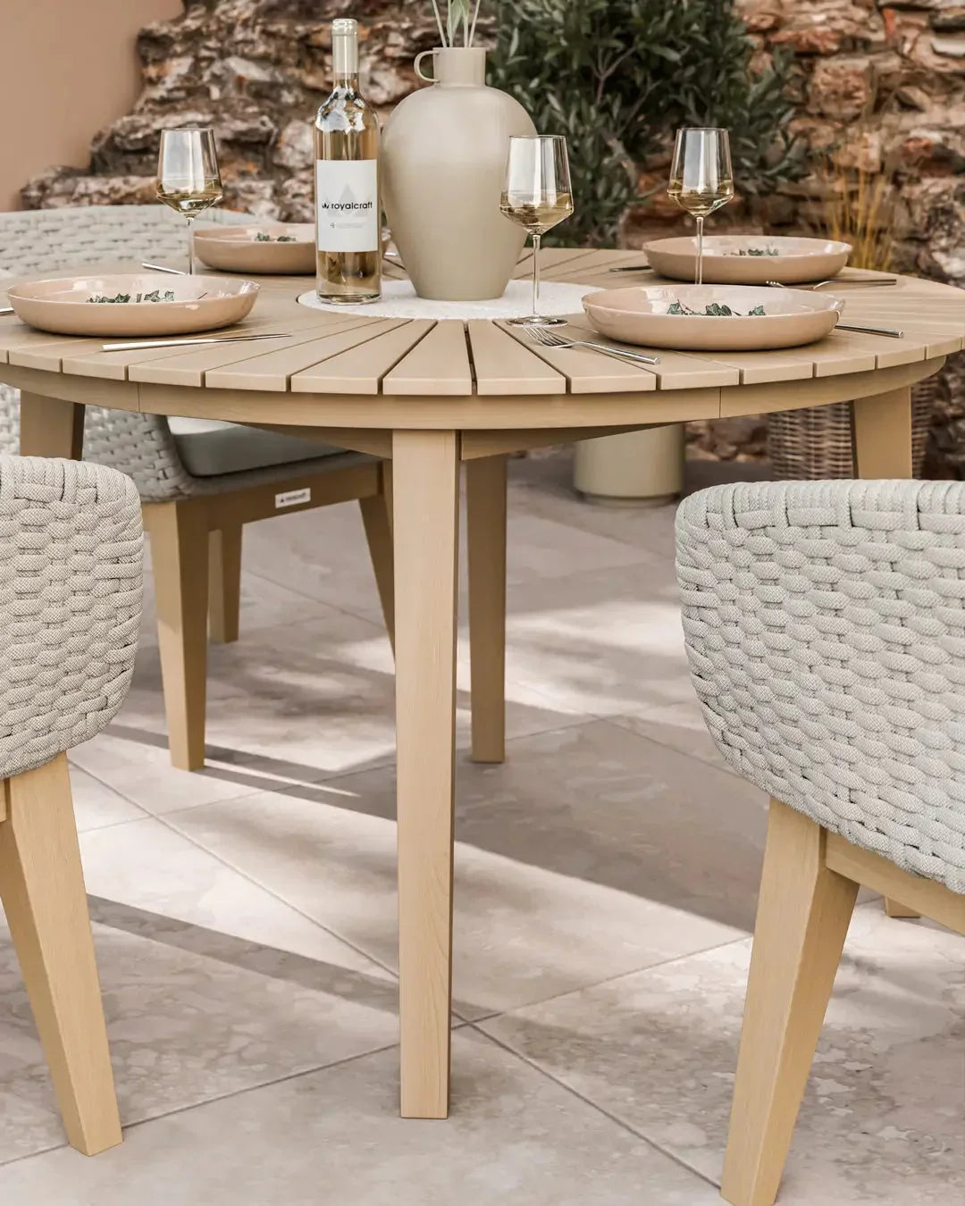 Round wooden outdoor dining table with beige rope chairs set for four on patio tiles