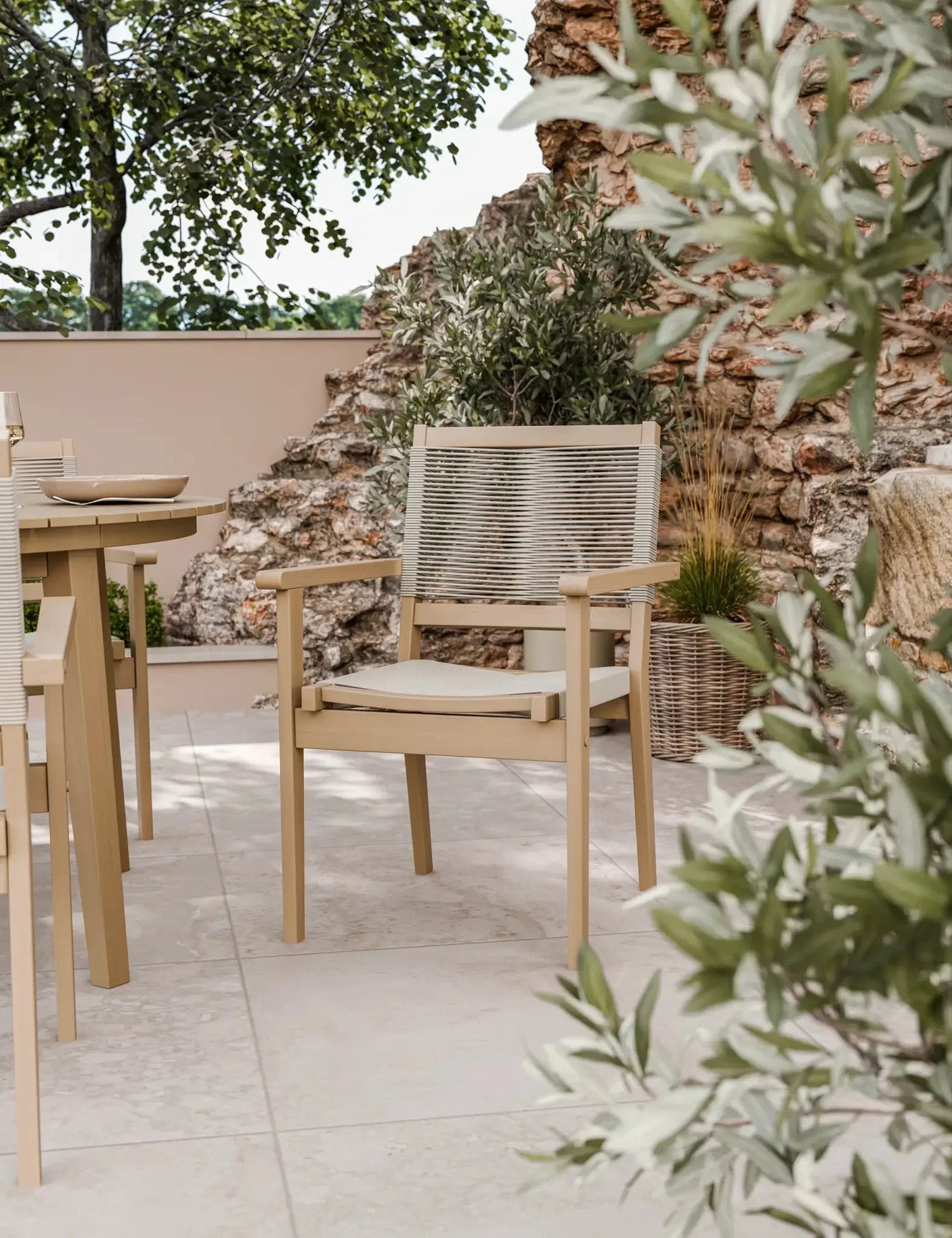 Beige outdoor dining chair with woven rope backrest and seat cushion on stone patio