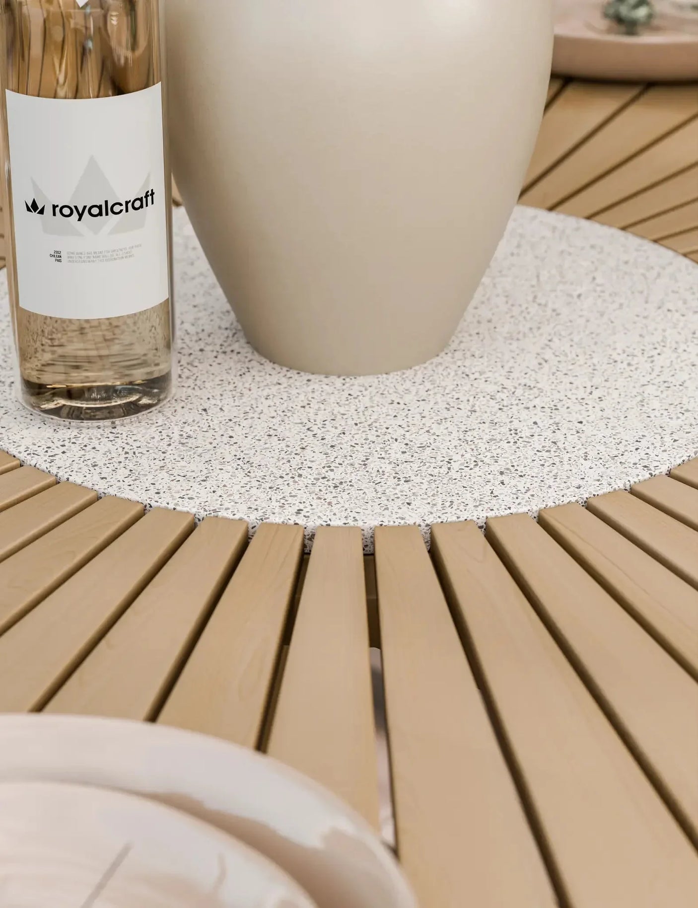 Round slatted wood dining table with speckled stone centrepiece and beige vase