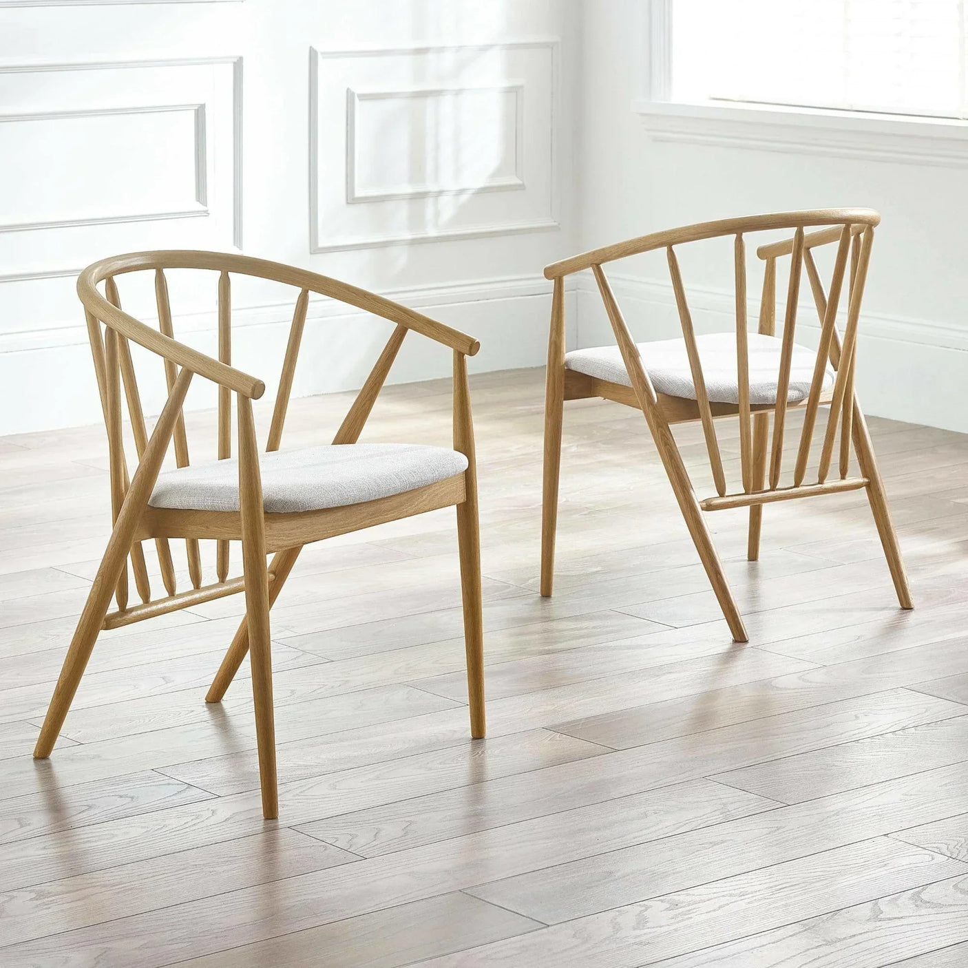 Pair of wooden dining chairs with curved backs and light fabric seats on wood floor