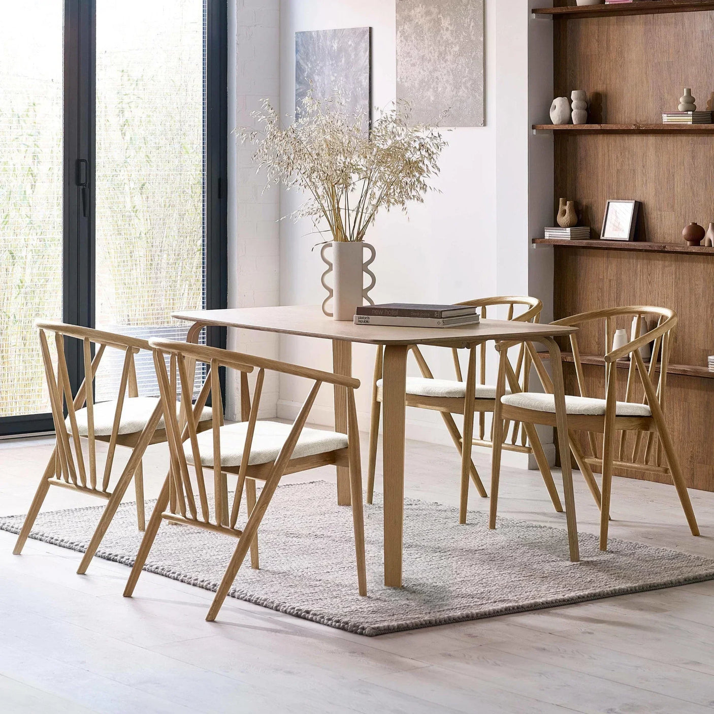 Light wood dining table set with four chairs on a grey rug in modern dining room