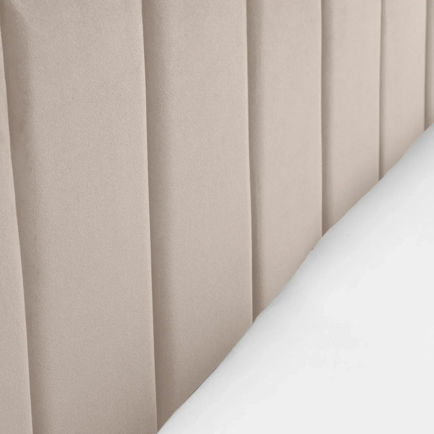 Beige velvet upholstered headboard with vertical panel design beside white bedding
