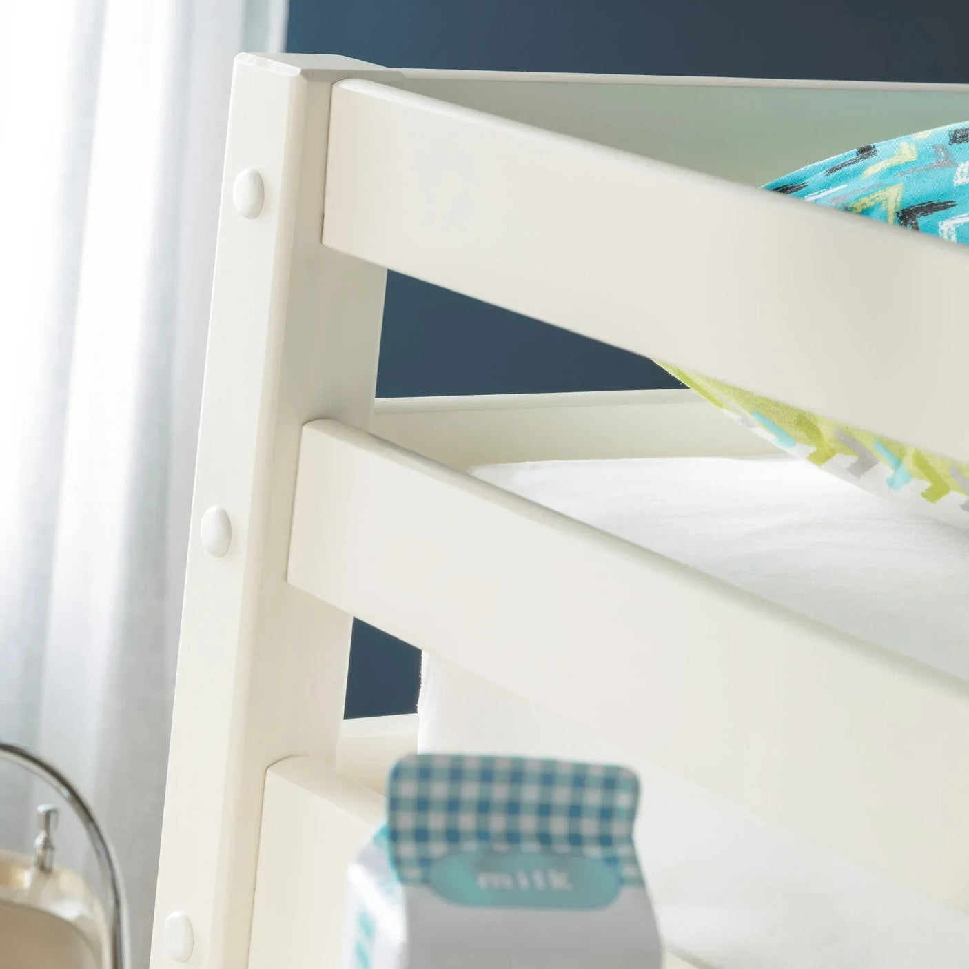 Close-up of white wooden bunk bed frame with safety rails and colorful pillow