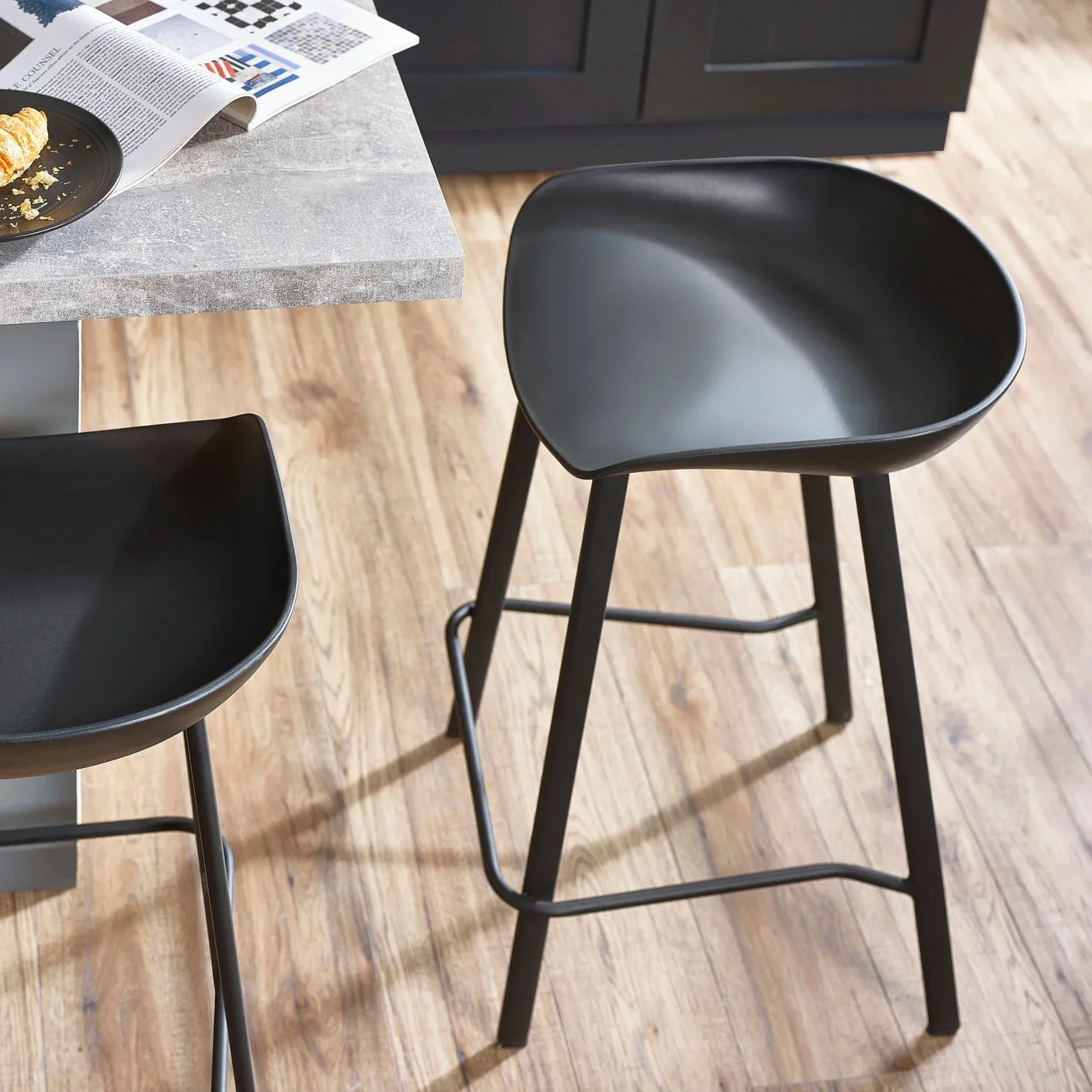 Black bar stool with curved seat and metal legs beside kitchen counter on wood flooring