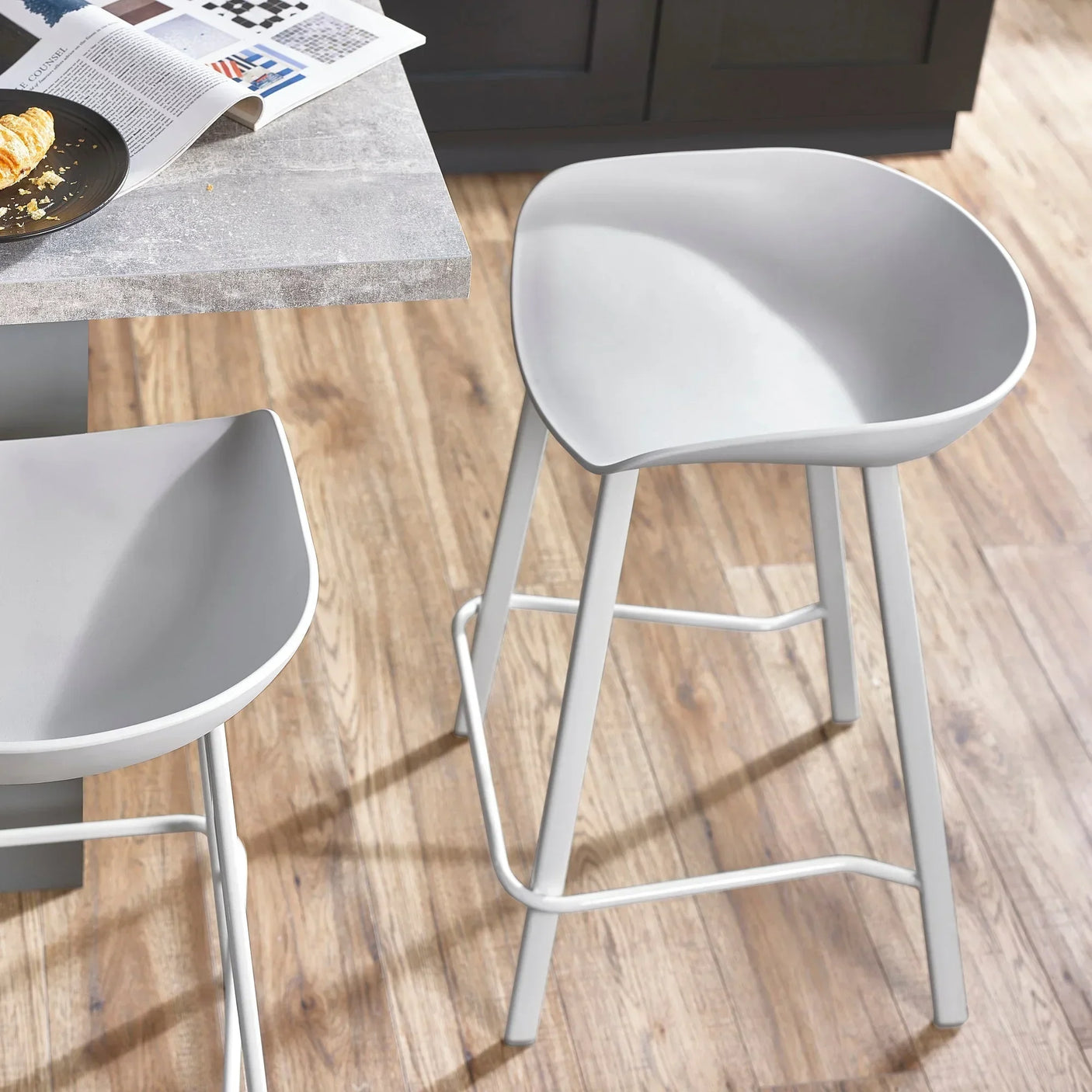 Grey bar stools with curved seats beside a light stone kitchen counter on wooden flooring