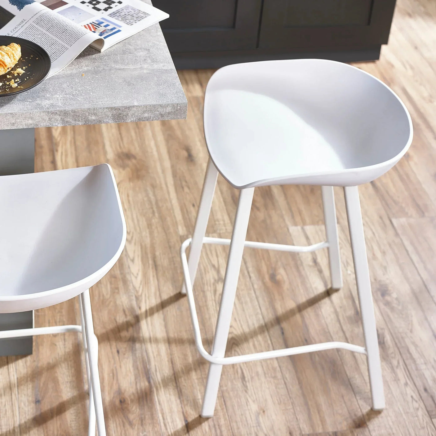 White bar stool with curved seat and metal legs beside a kitchen counter on wood flooring