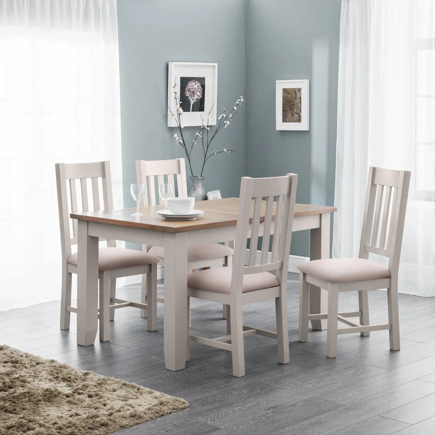 Wood dining table with four matching chairs in bright room with grey walls and framed art