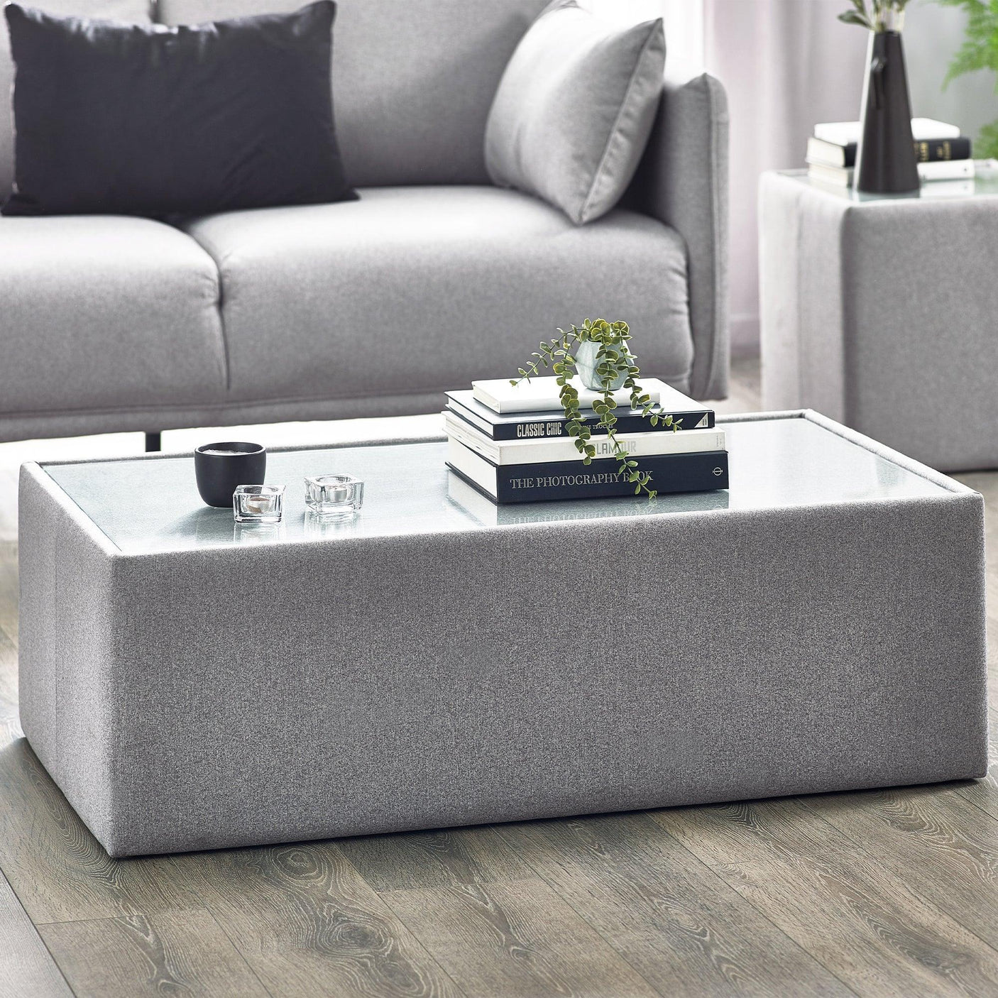 Grey upholstered coffee table with glass top and decor in modern living room setting