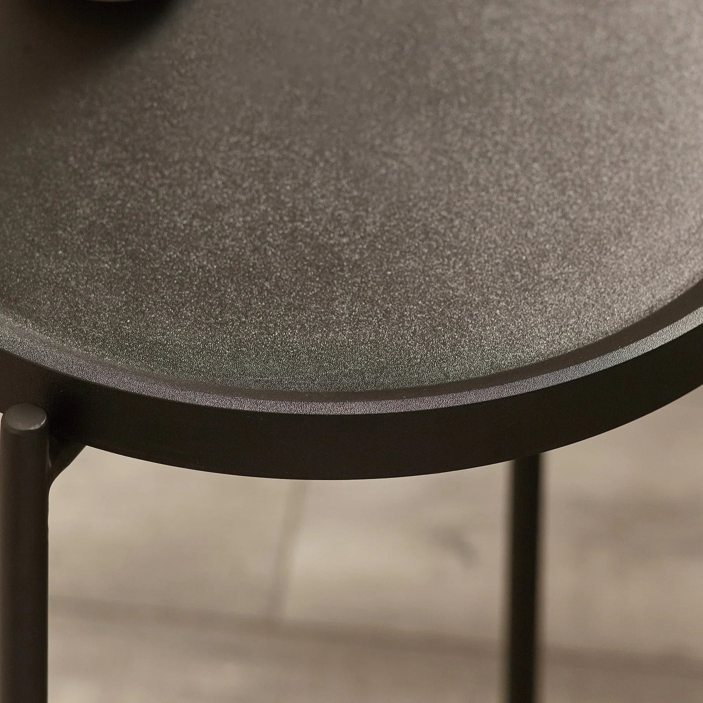 Round black metal side table with textured top and slim legs on wooden floor