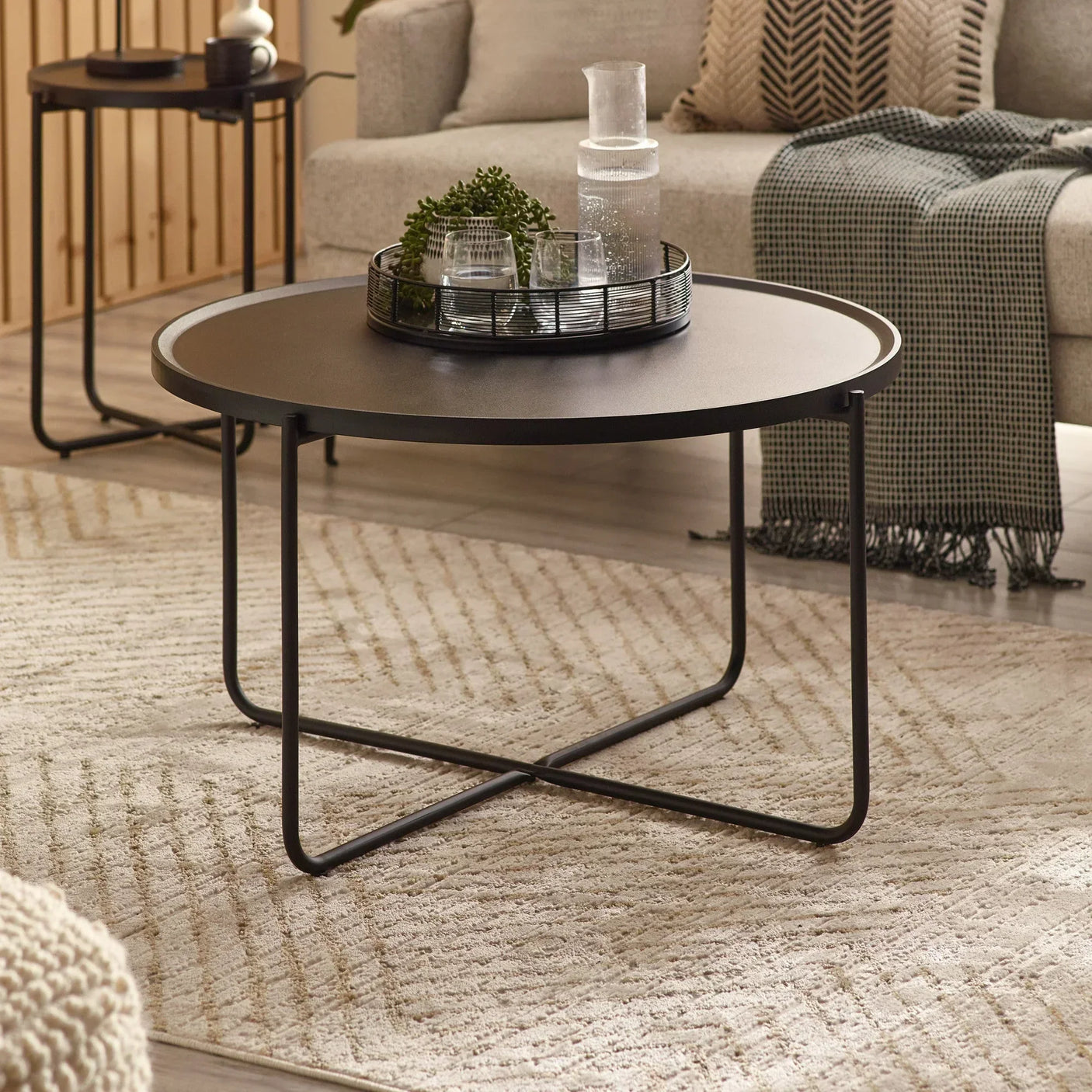 Round black metal coffee table with cross legs in modern living room setting