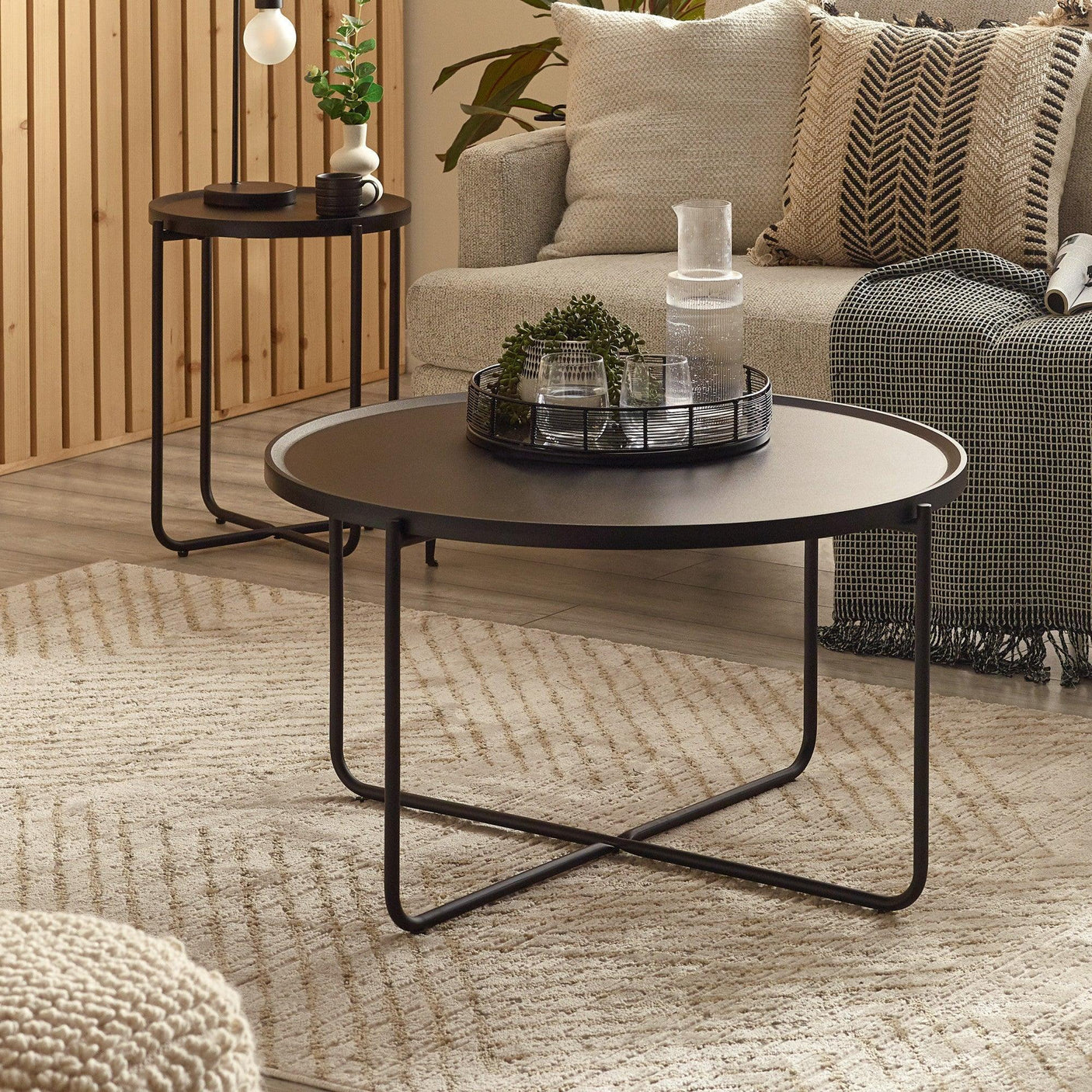 Round black metal coffee table with thin legs in modern living room on striped rug