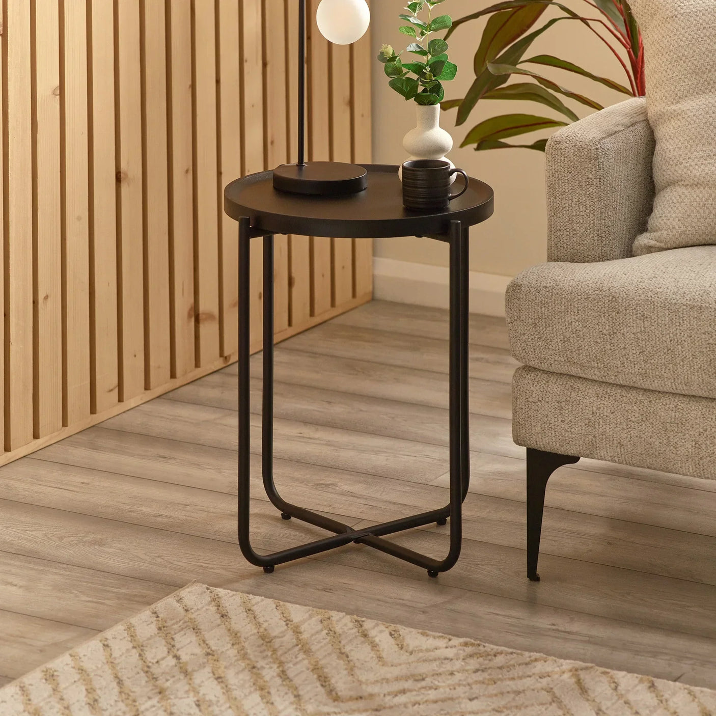 Black metal side table with round top beside beige sofa on wooden floor