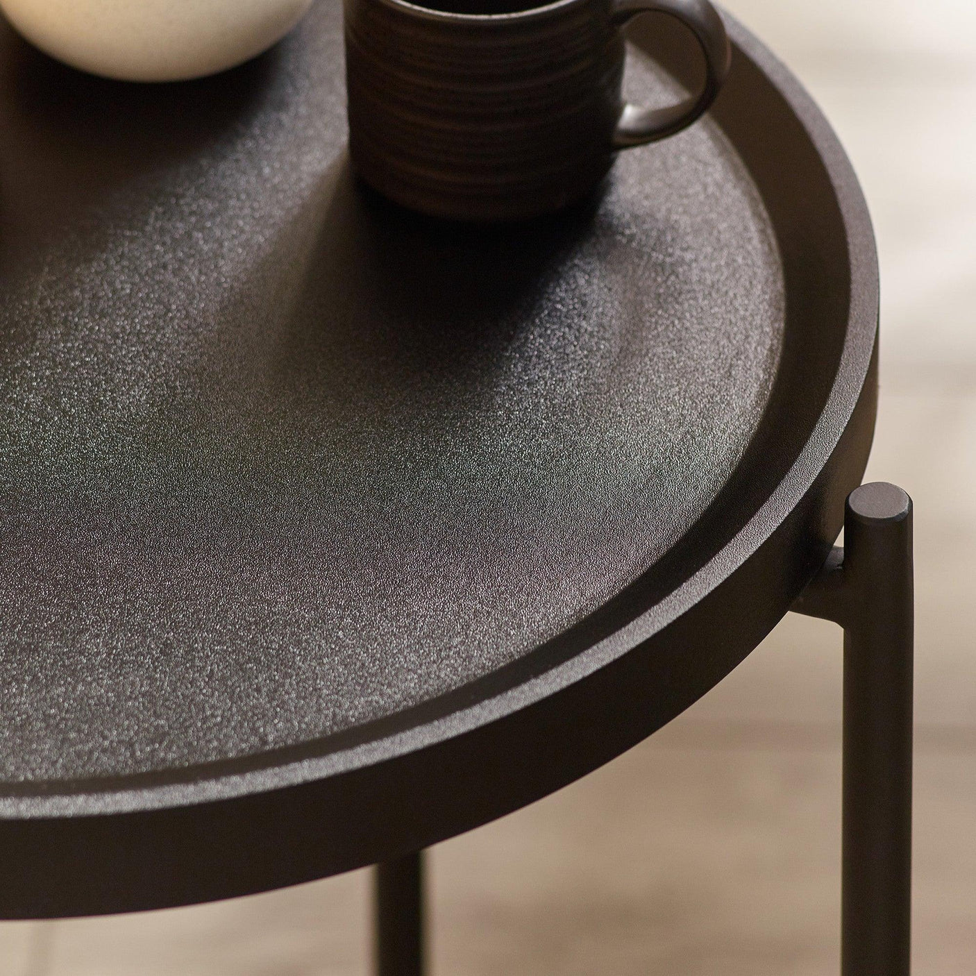 Round black metal side table with raised edge and ceramic mugs on surface
